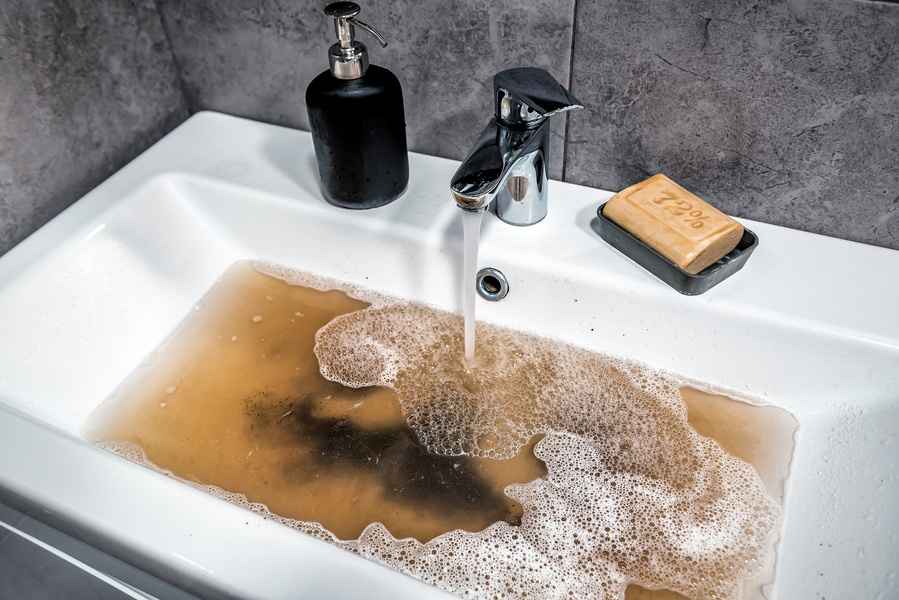 Clogged bathroom sink filled with dirty water