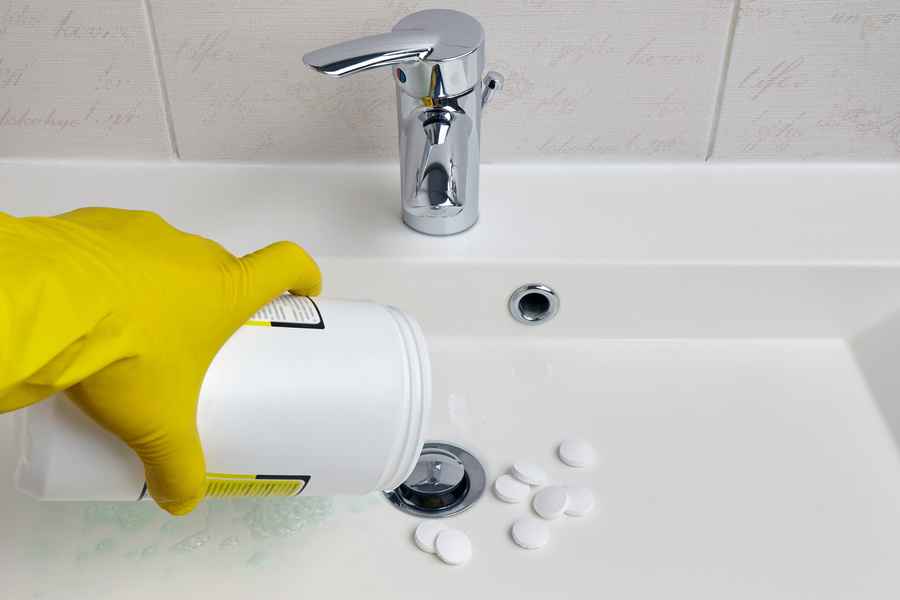 Man disinfecting and cleaning the his bathroom sink with detergent granules to get rid of sewer smells