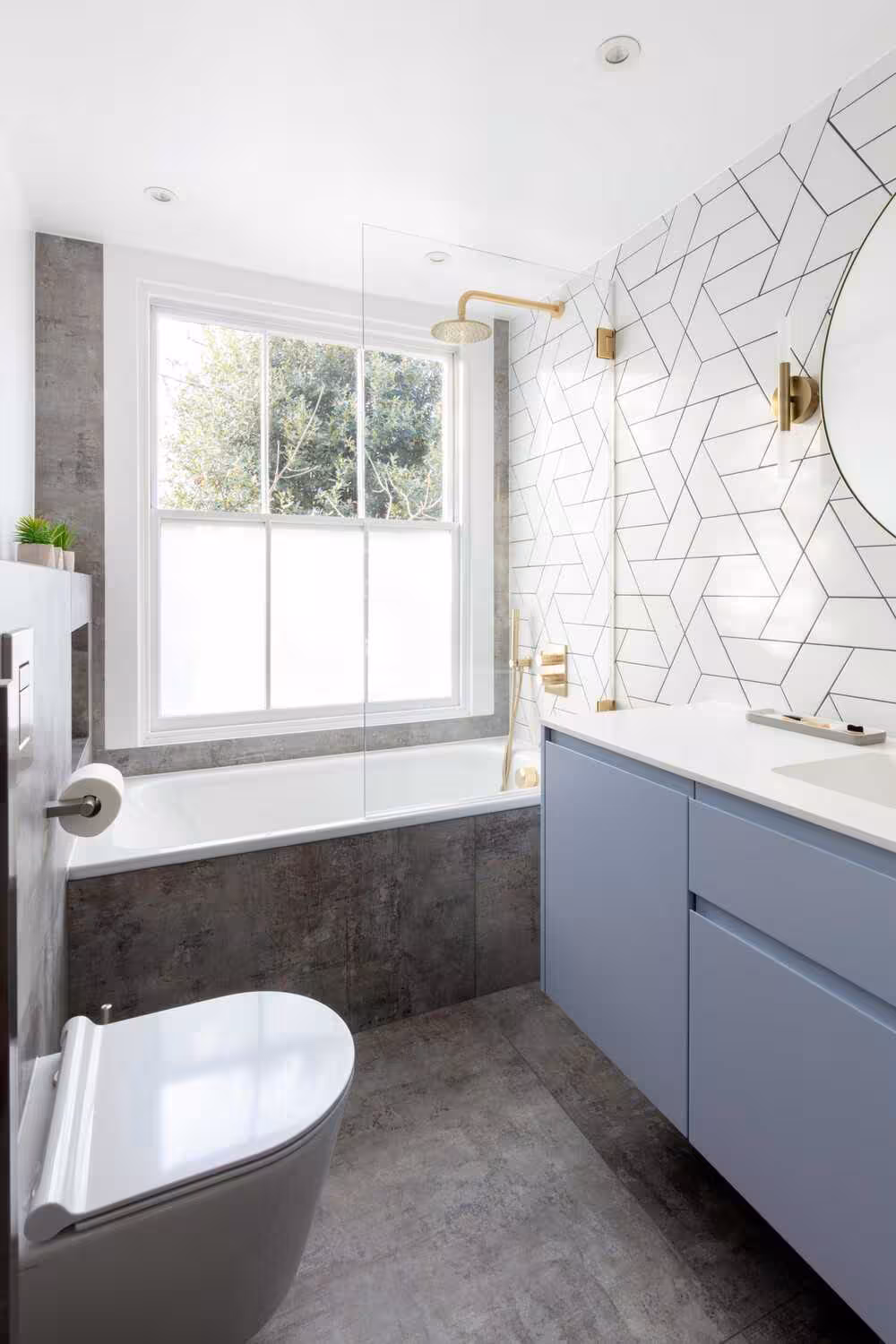 Pastel blue gray bathroom vanity with a beautiful geometric tile backslash with gold hardware, a toilet system, and bathtub
