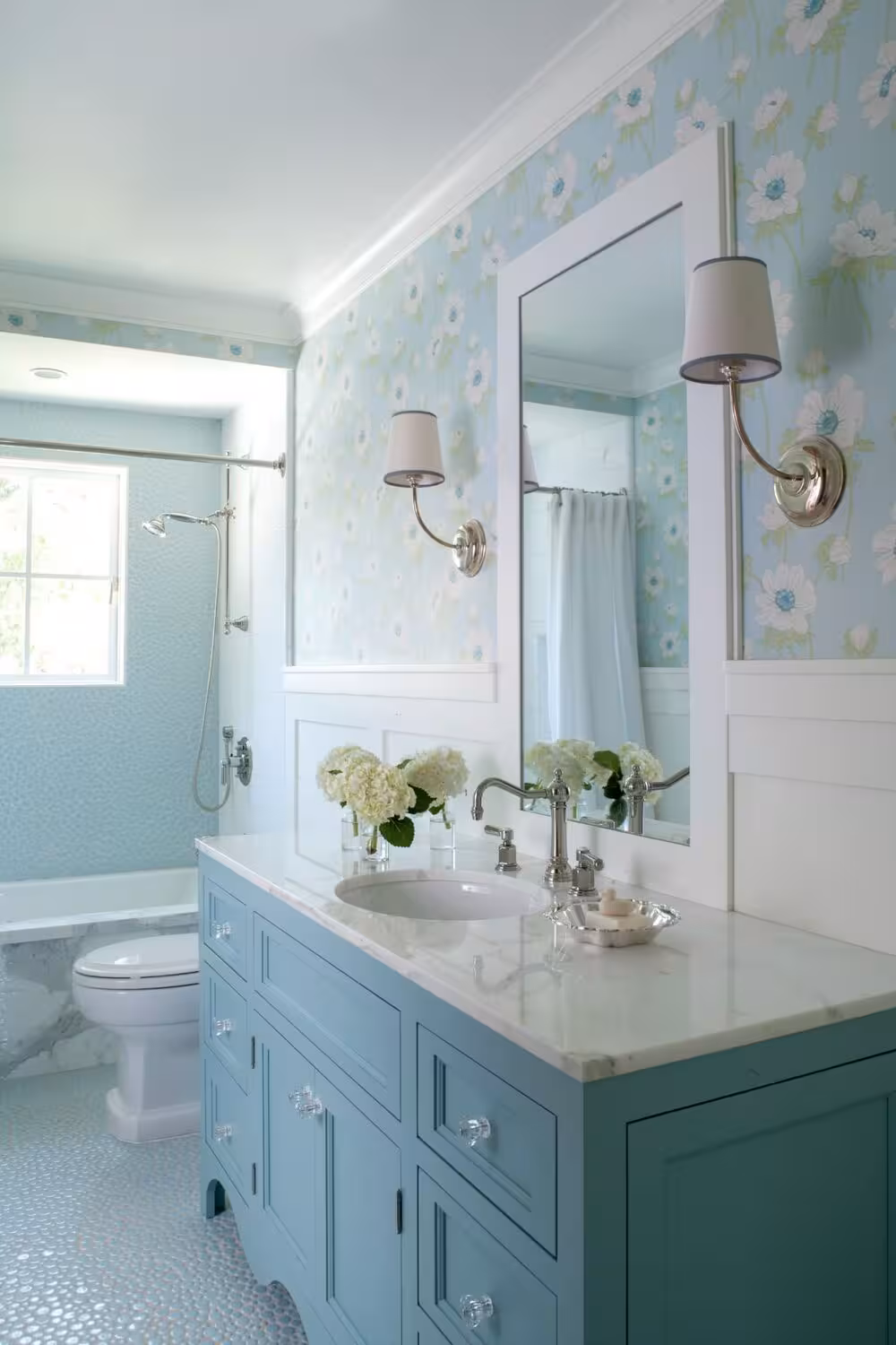 Teal bathroom cabinet with a white burble wall tiles and wallpaper above wainscot.