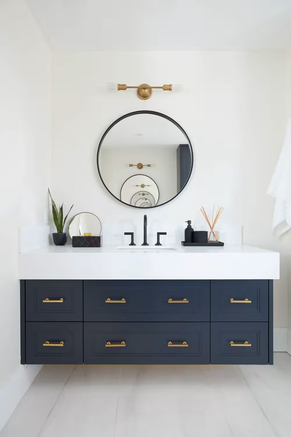 Dark blue bathroom vanity ideas with brass hardwares and a round center mirror