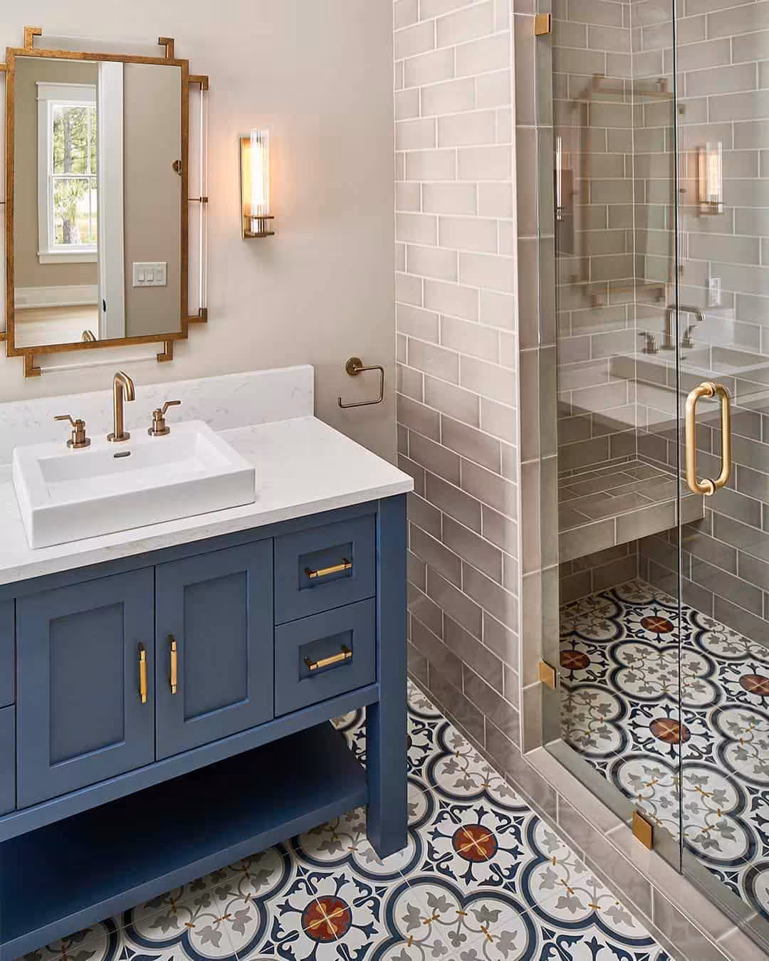 Navy blue bathroom vanity with gold hardware, a white marble countertop, subway wall tiles, mosaic floor, and wall mirror.