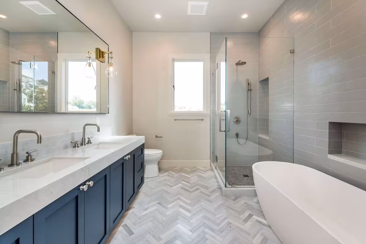 A navy blue bathroom vanity with a white countertop and brass hardwares with a freestanding tub by the right.