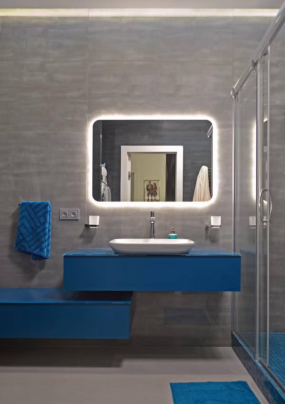 Blue vanity bathroom with backlite mirror, blue towel, and rug