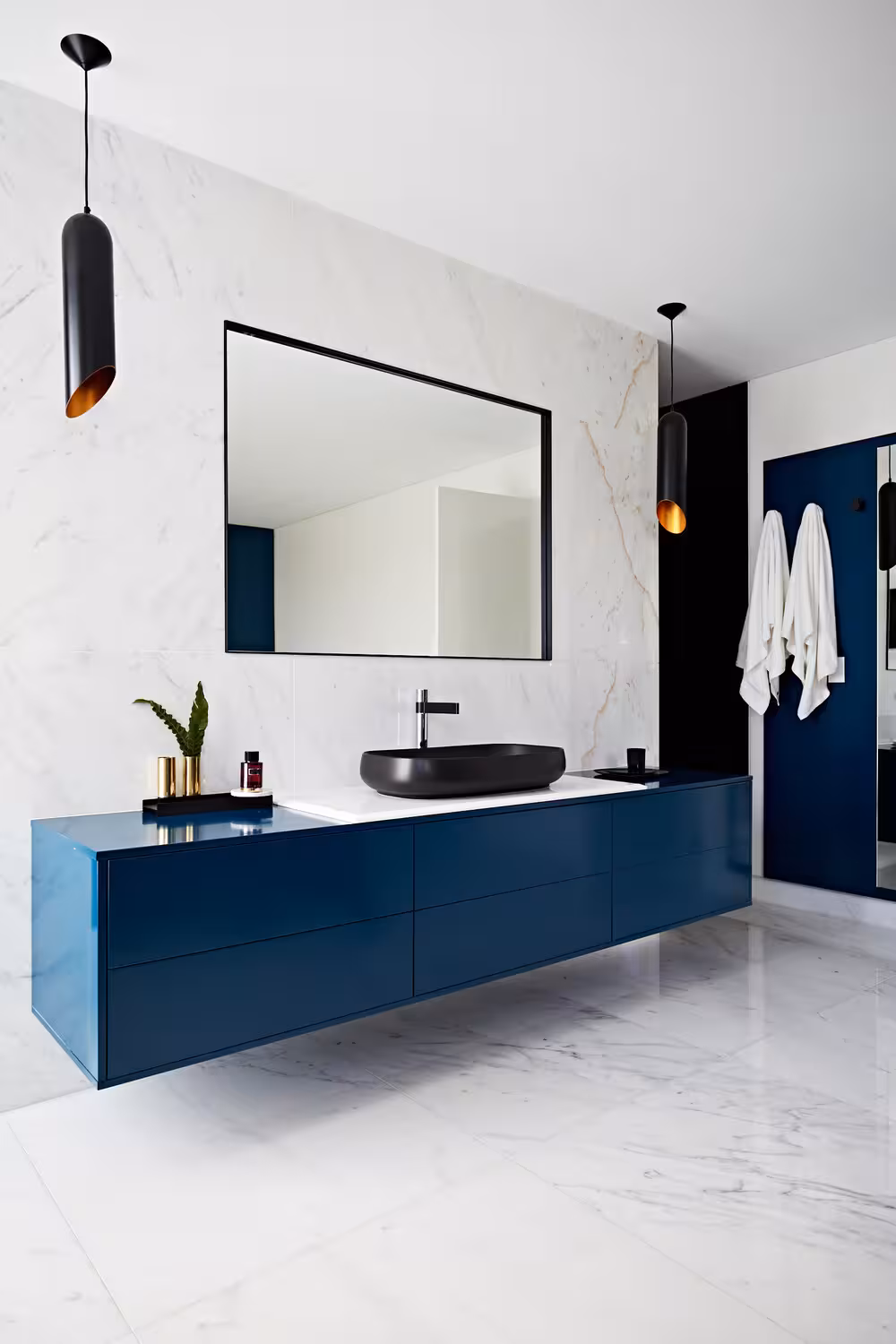 Blue vanity with floating shelve, a black sink and pendant lights