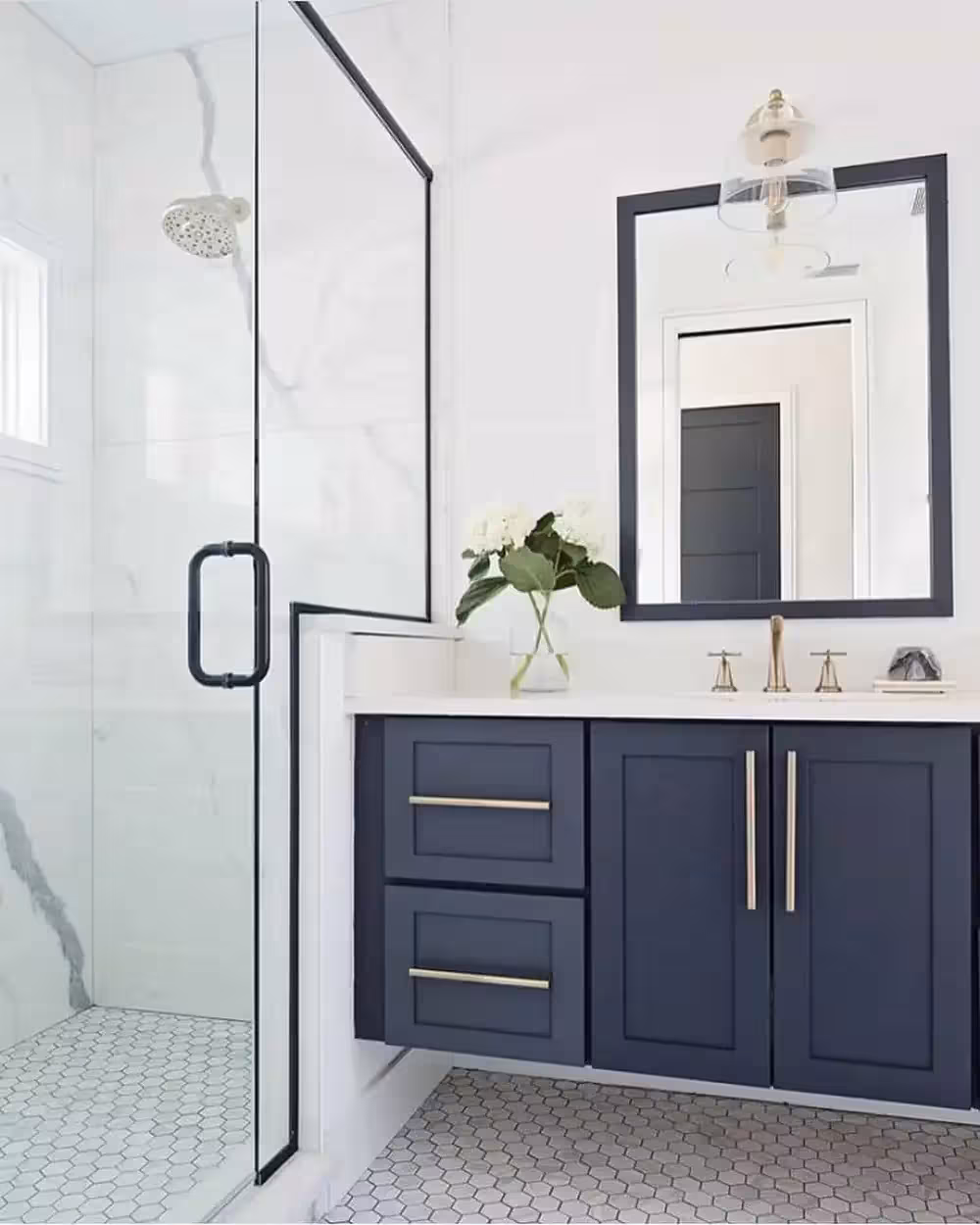 Floating Navy blue Vanity by the entrace of the shower with a wall mirror and a flower on the countertop