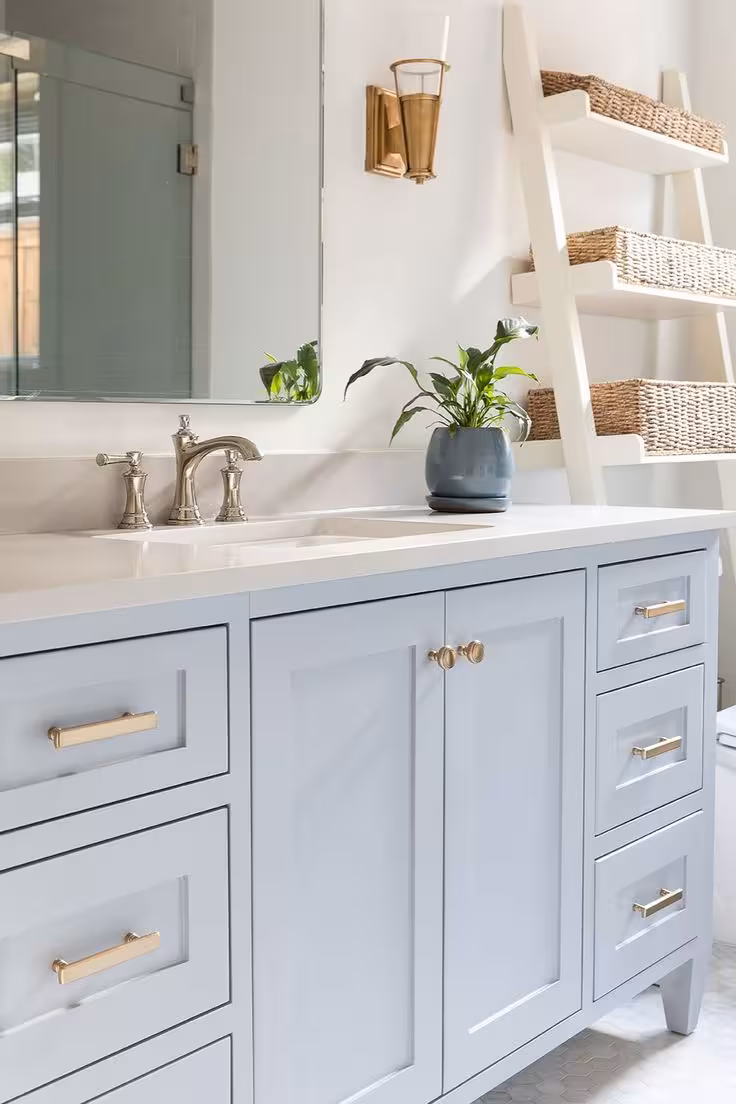 Soft light blue bathroom vanity with a flower on the countertop and a step of baskets and wall mirror