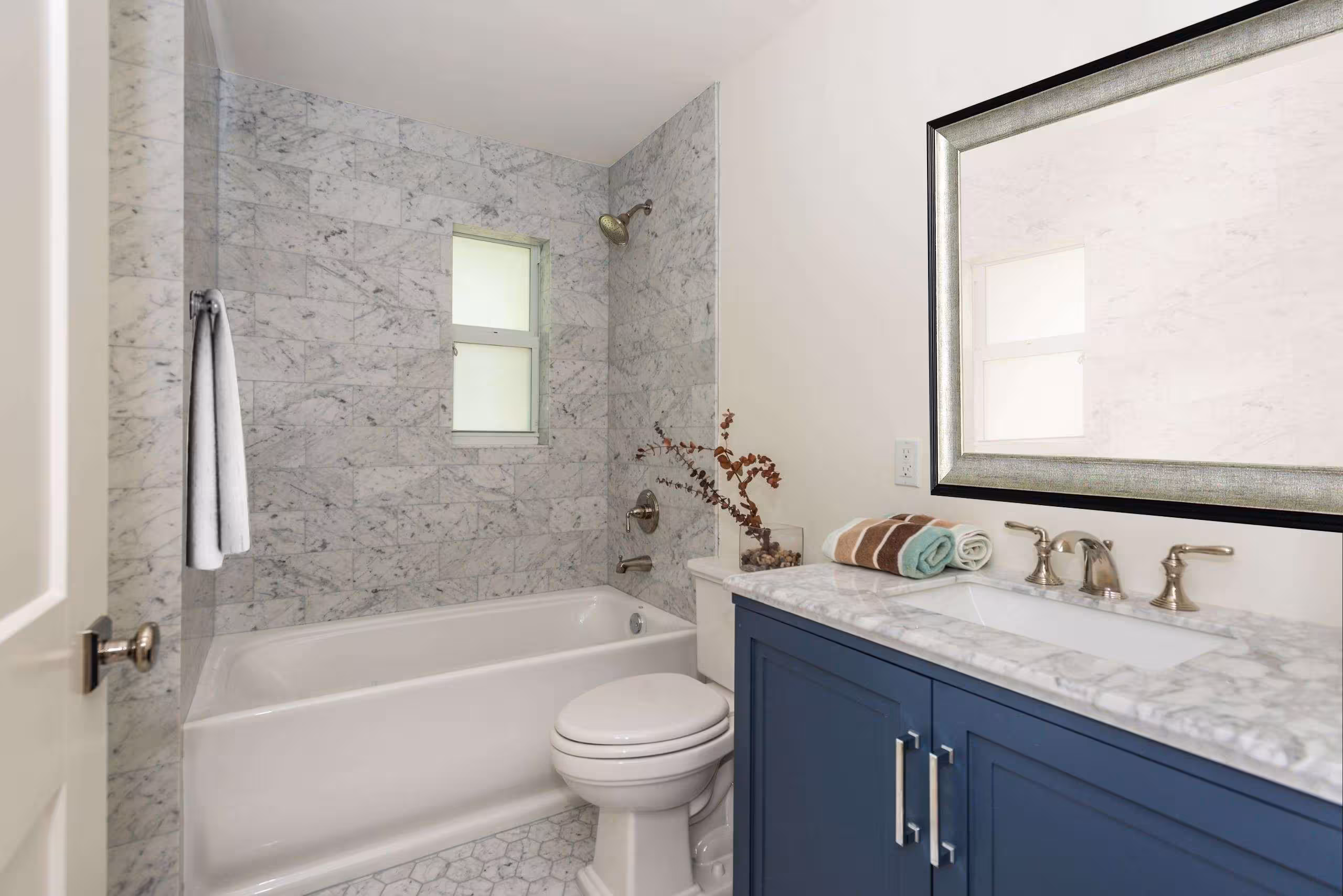Blue bathroom vanity with a stone sink, a toilet, bathrub, and marble tiles