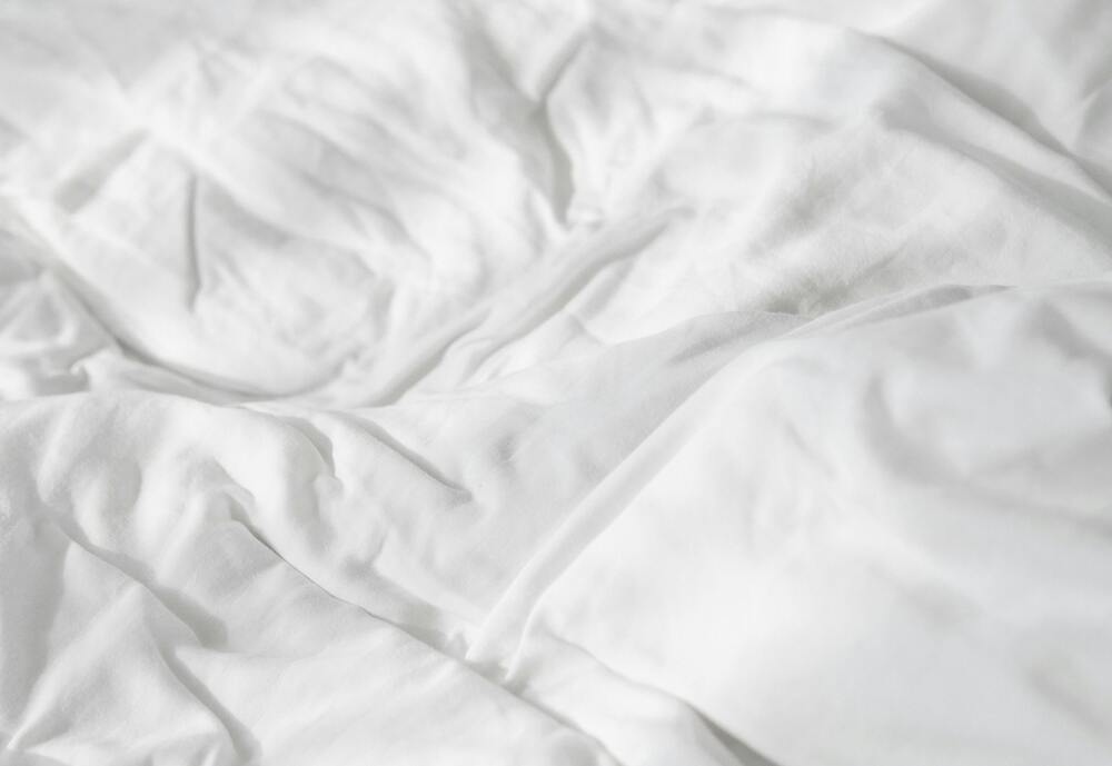 Unfolded cotton bed sheet on bed